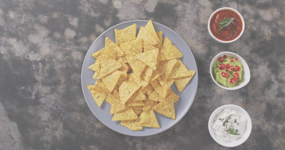 Blue Plate Stacked with Tortilla Chips and Trio of Salsa Guacamole Sour Cream Dips Flatlay