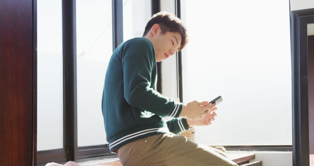 Teenager Relaxing with Smartphone by Window at Home - Free Images, Stock Photos and Pictures on Pikwizard.com