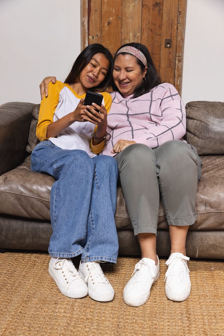 Happy Mother and Daughter Bonding and Smiling Using Smartphone at Home