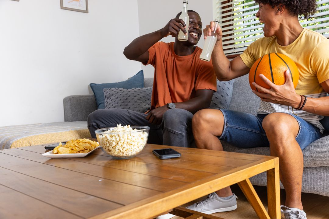 Clinking bottles while holding basketball on couch celebrating game night with snacks