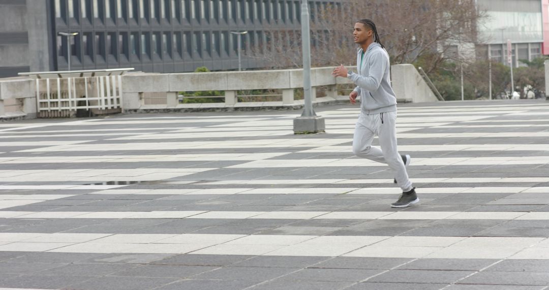 Man jogging across patterned urban plaza in grey tracksuit and sneakers