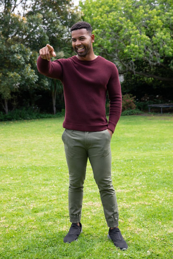 Casual Young Man Pointing and Smiling in Scenic Park Setting