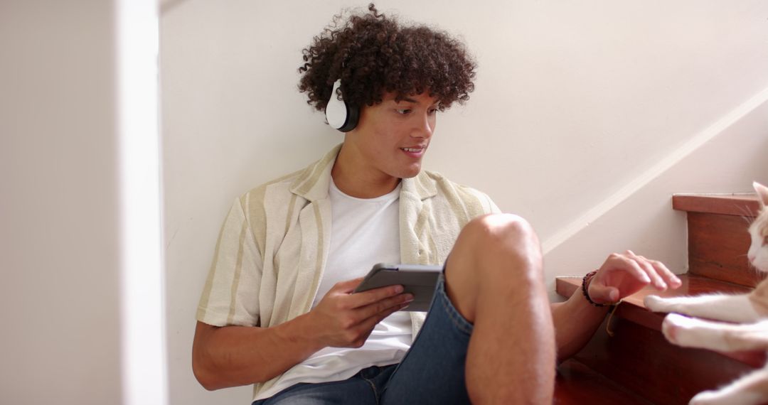 Young Man Relaxing with Headphones and Tablet Petting Cat at Home