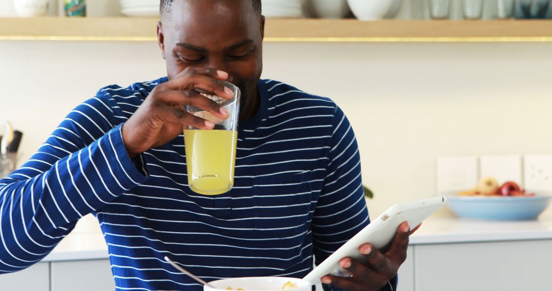 Smiling Man Drinking Juice and Using Digital Tablet at Breakfast - Free Images, Stock Photos and Pictures on Pikwizard.com