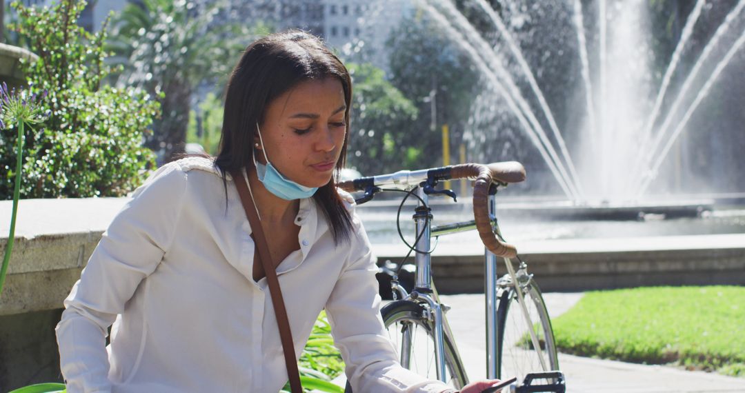 Woman taking a break from cycling at urban park fountain - Free Images, Stock Photos and Pictures on Pikwizard.com