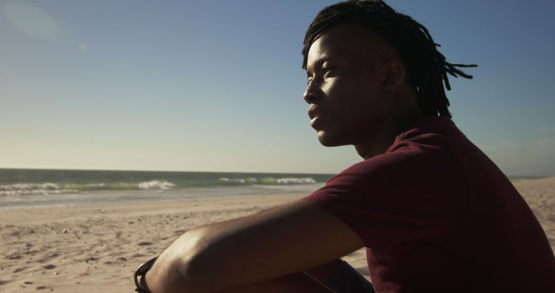 Contemplating on Sunny Beach: Young Man with Dreadlocks Watching Waves