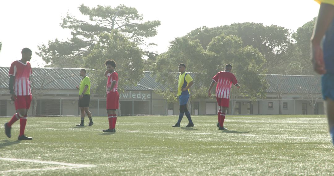 Soccer Players Competing on Sunny Field with Trees in Background