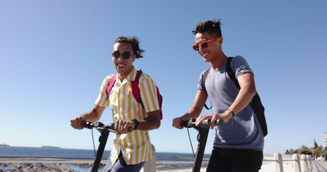 Two Young Men Riding Electric Scooters by Ocean on Sunny Day - Free Images, Stock Photos and Pictures on Pikwizard.com