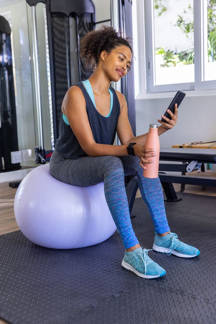 Fit Woman Balancing on Exercise Ball with Smartphone in Gym
