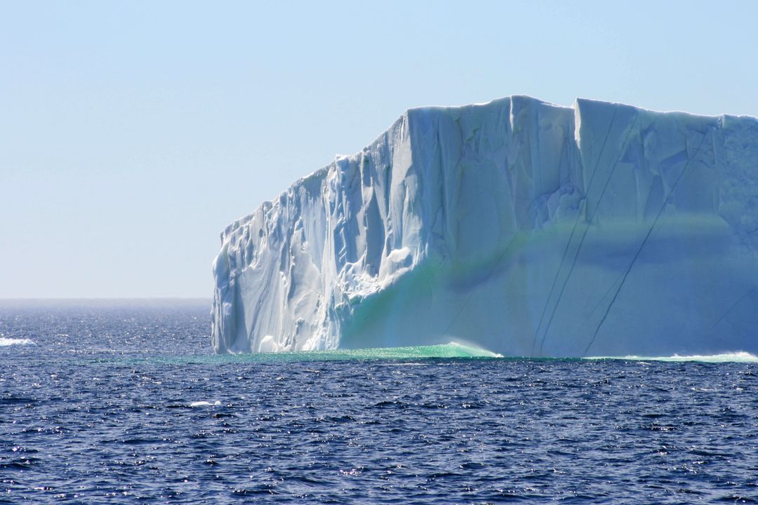 Towering Iceberg Floating in Deep Blue Ocean with Emerald Underwater Glow