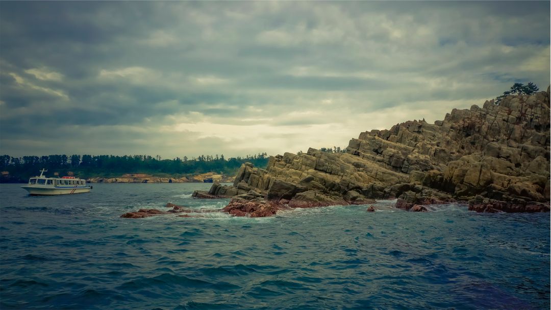 Scenic coastal view with rocky shoreline and boat on cloudy day - Free Images, Stock Photos and Pictures on Pikwizard.com