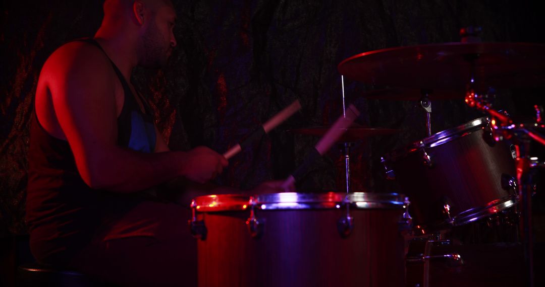 Musician Drumming Under Red Stage Lights in Dark Setting - Free Images, Stock Photos and Pictures on Pikwizard.com