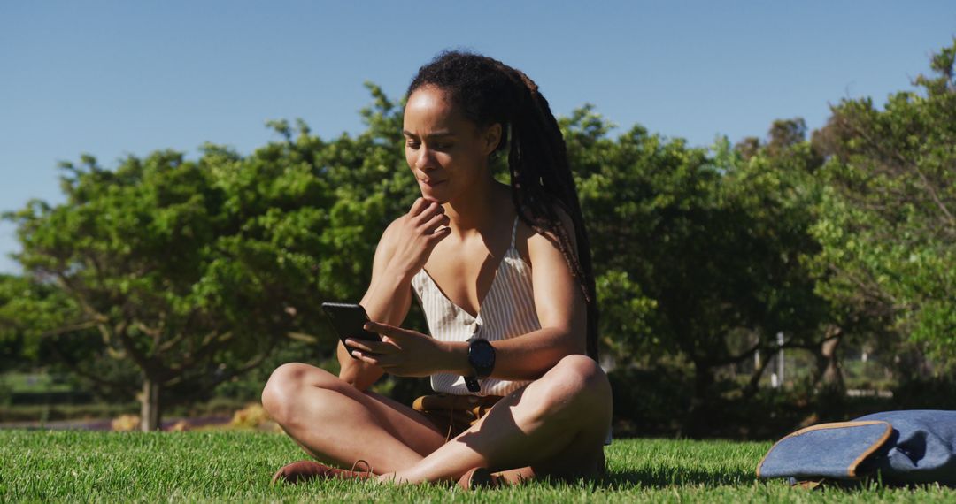 African American Woman Relaxing Outdoors with Smartphone in Nature - Free Images, Stock Photos and Pictures on Pikwizard.com