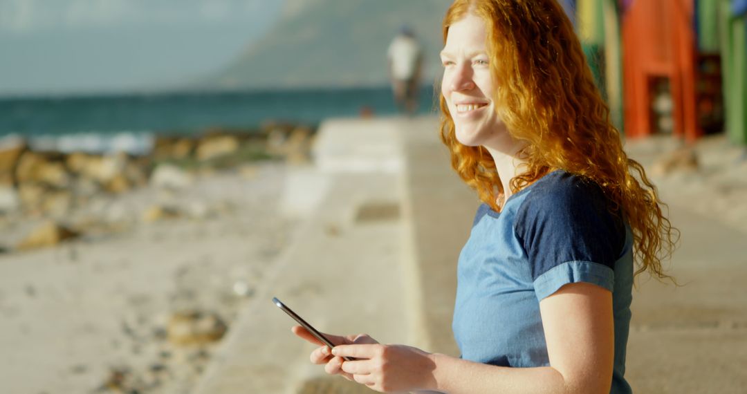 Smiling Redhead Woman Using Smartphone at Beach on Sunny Day - Free Images, Stock Photos and Pictures on Pikwizard.com