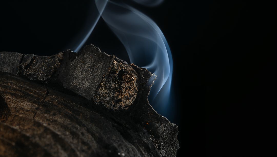 Smoldering Charred Log Emitting Blue Smoke Plumes and Ember Glow over Dark Background