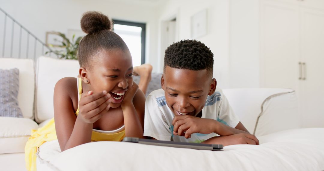 Joyful Siblings Watching Tablet on Sofa at Home