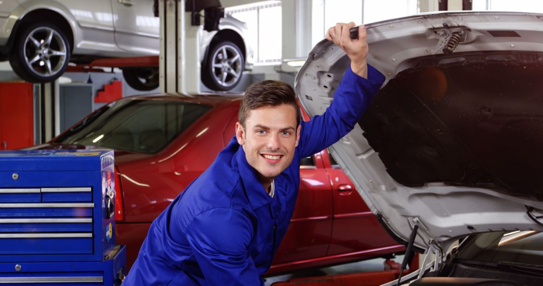 Smiling Mechanic in Blue Overalls Fixing Car in Busy Auto Repair Shop - Free Images, Stock Photos and Pictures on Pikwizard.com