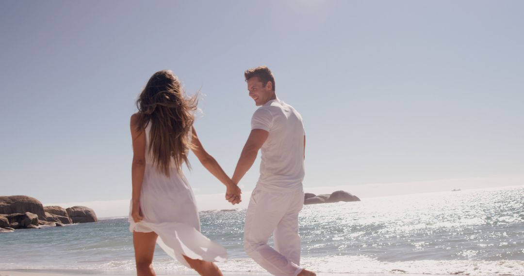 Happy Couple Walking on Sunny Beach Hand in Hand - Free Images, Stock Photos and Pictures on Pikwizard.com