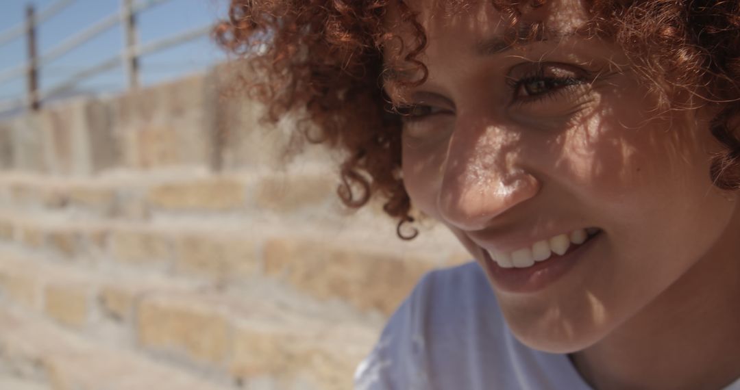 Happy Woman with Curly Hair Smiling Outdoors in Sunlight - Free Images, Stock Photos and Pictures on Pikwizard.com