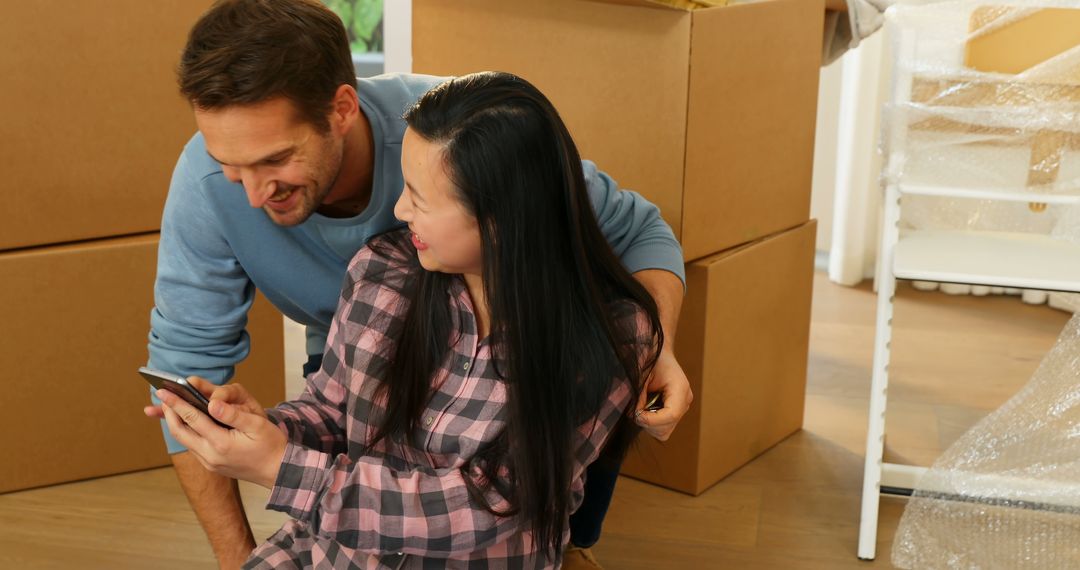 Couple Smiling at Phone in New Home with Moving Boxes