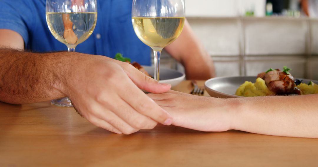 A Caucasian couple holds hands across a table set with wine and a meal, with copy space - Free Images, Stock Photos and Pictures on Pikwizard.com