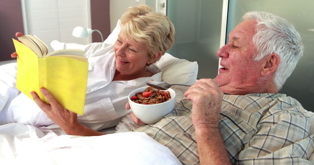 Senior Couple Relaxing in Bed Reading Book and Eating Breakfast - Free Images, Stock Photos and Pictures on Pikwizard.com