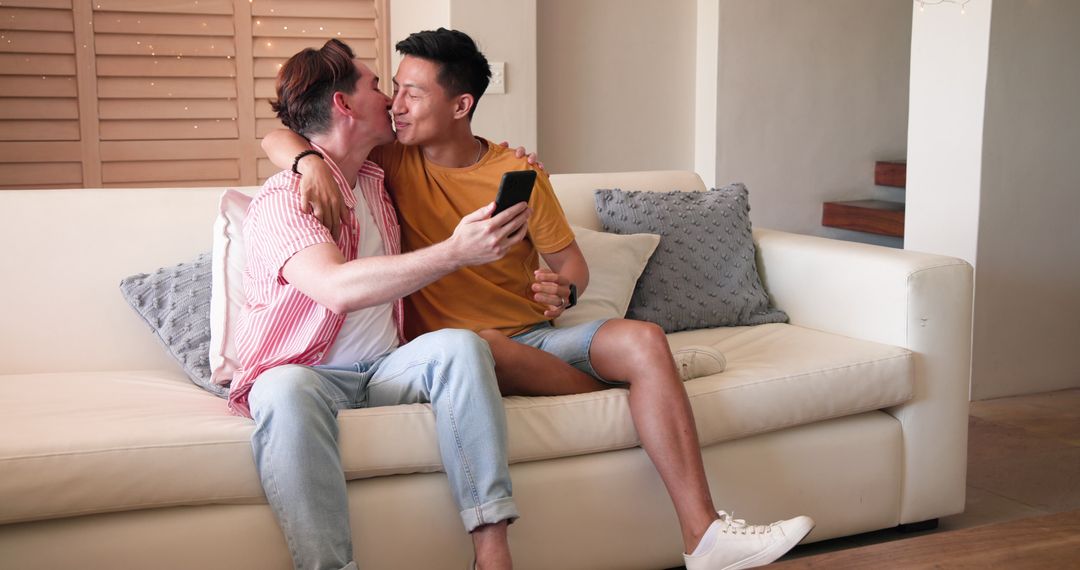 Happy Multicultural Couple Sharing Embrace on Couch with Smartphone