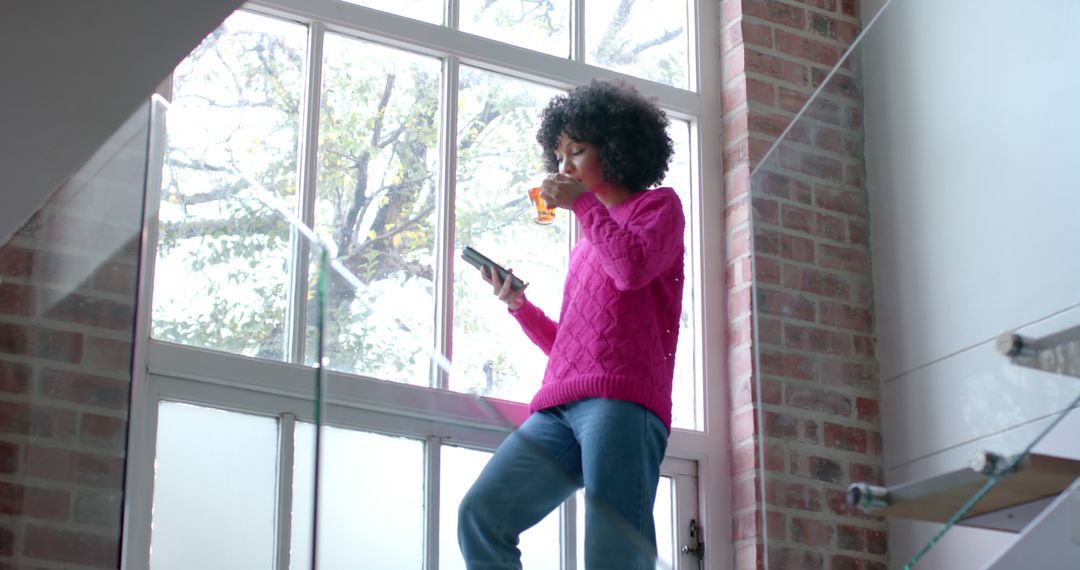 Woman Drinking Juice and Using Phone Near Sunlit Brick Wall - Free Images, Stock Photos and Pictures on Pikwizard.com