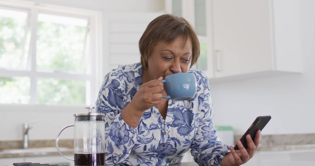 Middle Aged Woman Enjoying Coffee While Using Smartphone in Kitchen - Free Images, Stock Photos and Pictures on Pikwizard.com