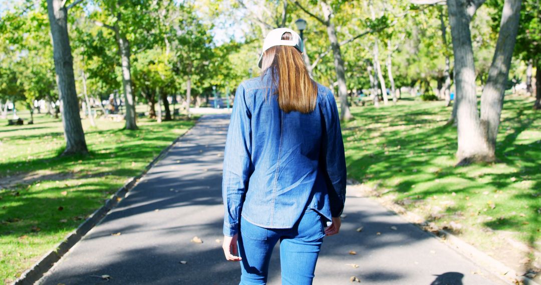 Back view of biracial woman with cap walking down alley in sunny park - Free Images, Stock Photos and Pictures on Pikwizard.com