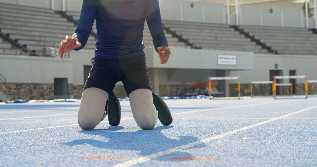 Athlete Kneeling on Blue Track in Sunlit Stadium - Free Images, Stock Photos and Pictures on Pikwizard.com