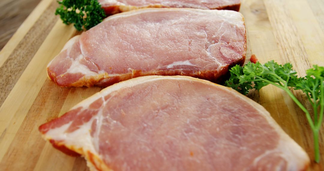 Fresh uncooked pork loin chops on wooden surface with parsley garnish - Free Images, Stock Photos and Pictures on Pikwizard.com