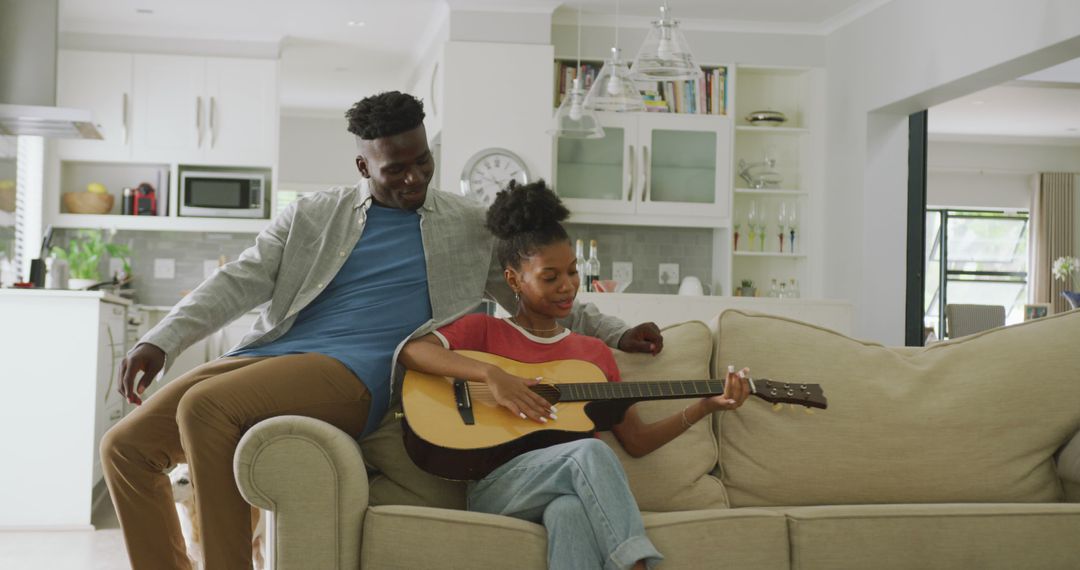 Image of happy african american couple sitting on sofa, singing and playing guitar - Free Images, Stock Photos and Pictures on Pikwizard.com