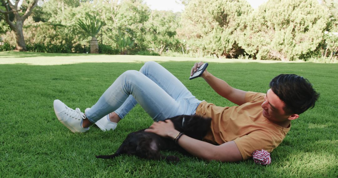 Man Relaxing with Dog in Park Holding Smartphone