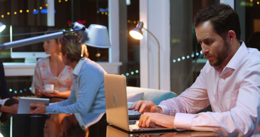 Businessman on Laptop in Modern Workspace with Conversing Colleagues