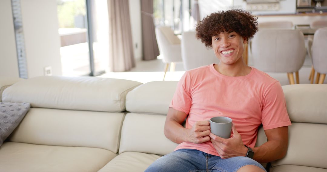 Cheerful Young Man Enjoying Coffee Break on Comfortable Sofa