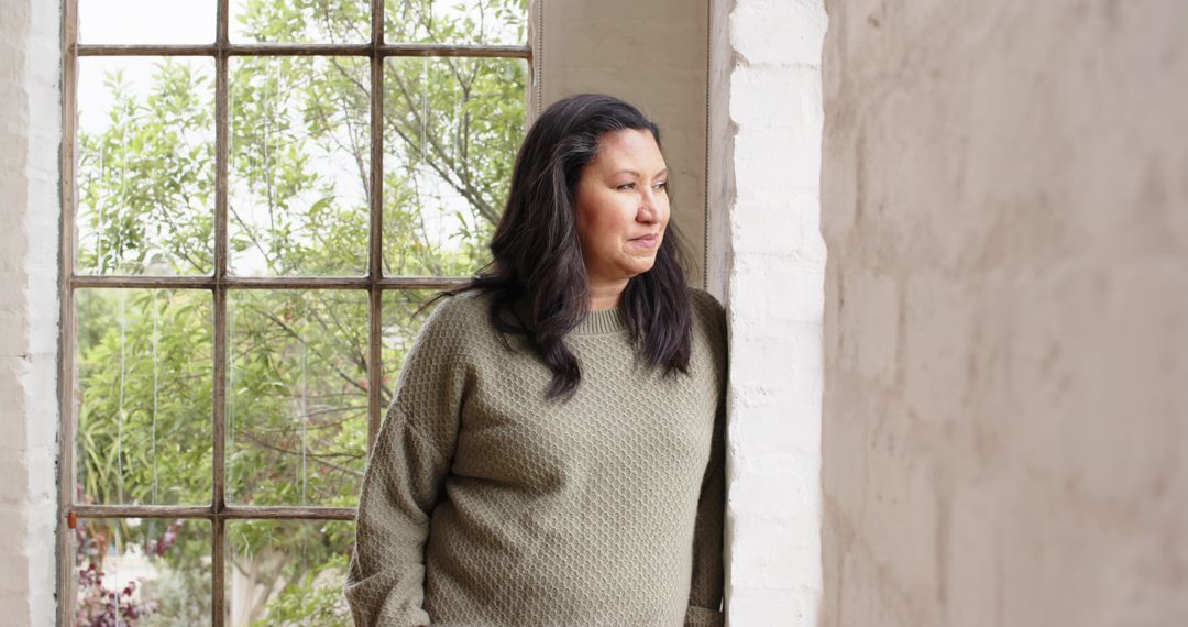 Thoughtful Woman Looking Out Bright Window with Foliage View