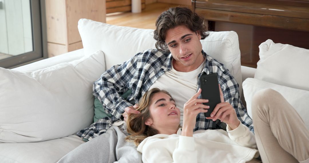 Relaxed Couple Using Smartphone on White Sofa at Home
