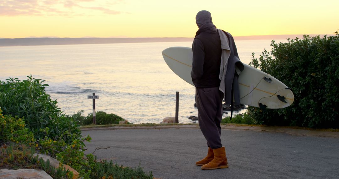 Surfer Standing On Coastal Road Holding Surfboard At Sunset - Free Images, Stock Photos and Pictures on Pikwizard.com