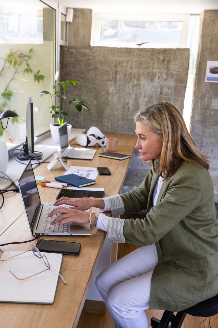 Senior Professional in Khaki Blazer Typing on Laptop in Modern Office
