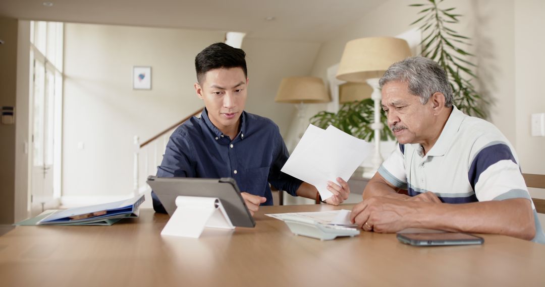 Young man assisting elderly man with paperwork at home - Free Images, Stock Photos and Pictures on Pikwizard.com