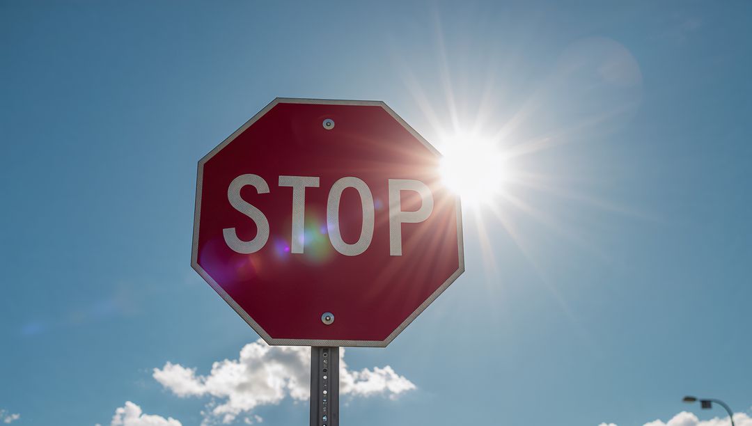Sunlit Red Stop Sign Reflecting Bright Sunlight with Lens Flare and Starburst