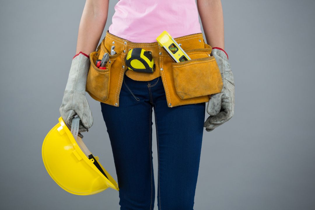 Woman with tool belt and holding hard hat against grey background - Free Images, Stock Photos and Pictures on Pikwizard.com