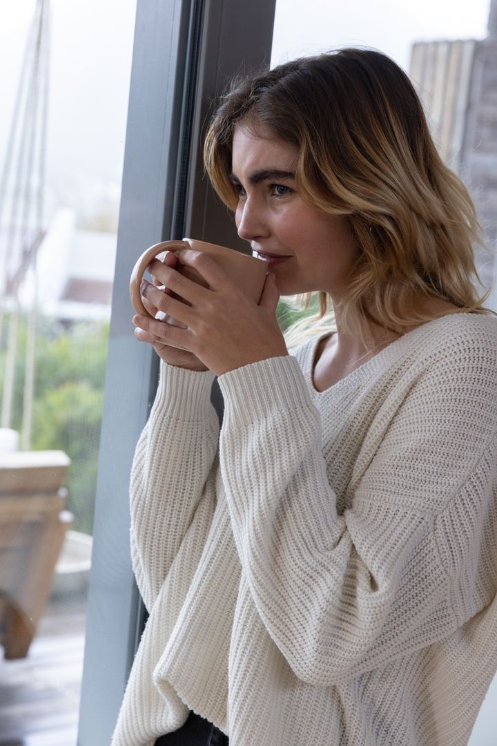 Serene Woman in Knit Sweater Enjoying Coffee by Window