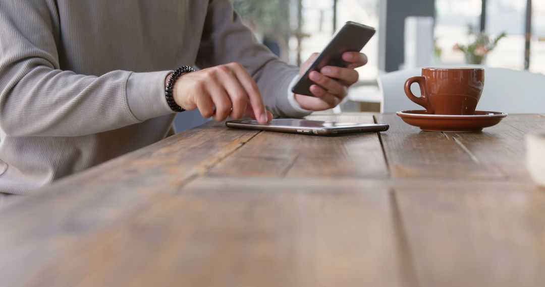 Person using smartphone and tablet at cafe table with coffee cup - Free Images, Stock Photos and Pictures on Pikwizard.com