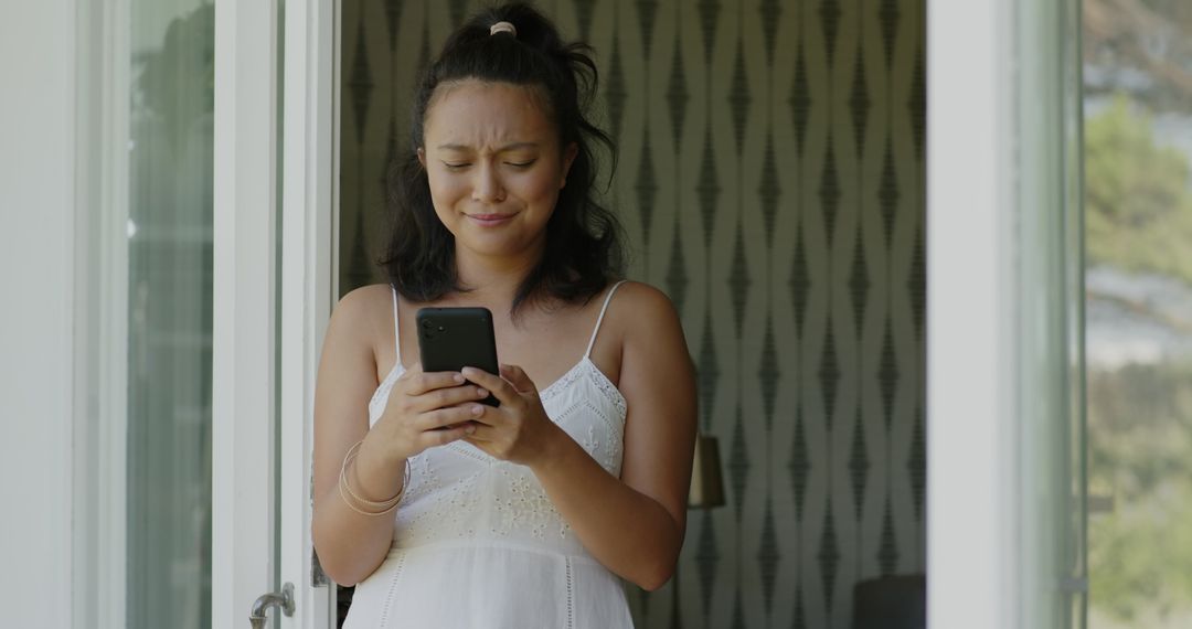 Asian Woman Smiling While Texting on Smartphone at Home