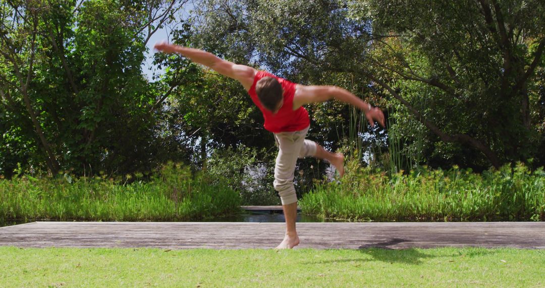Man Somersaulting on Jetty Near River and Forest Scenery
