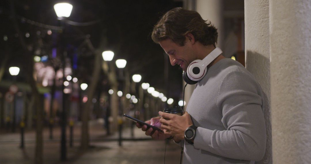 Man Enjoying Night Time Smartphone Browsing with Headphones in City Outdoors - Free Images, Stock Photos and Pictures on Pikwizard.com