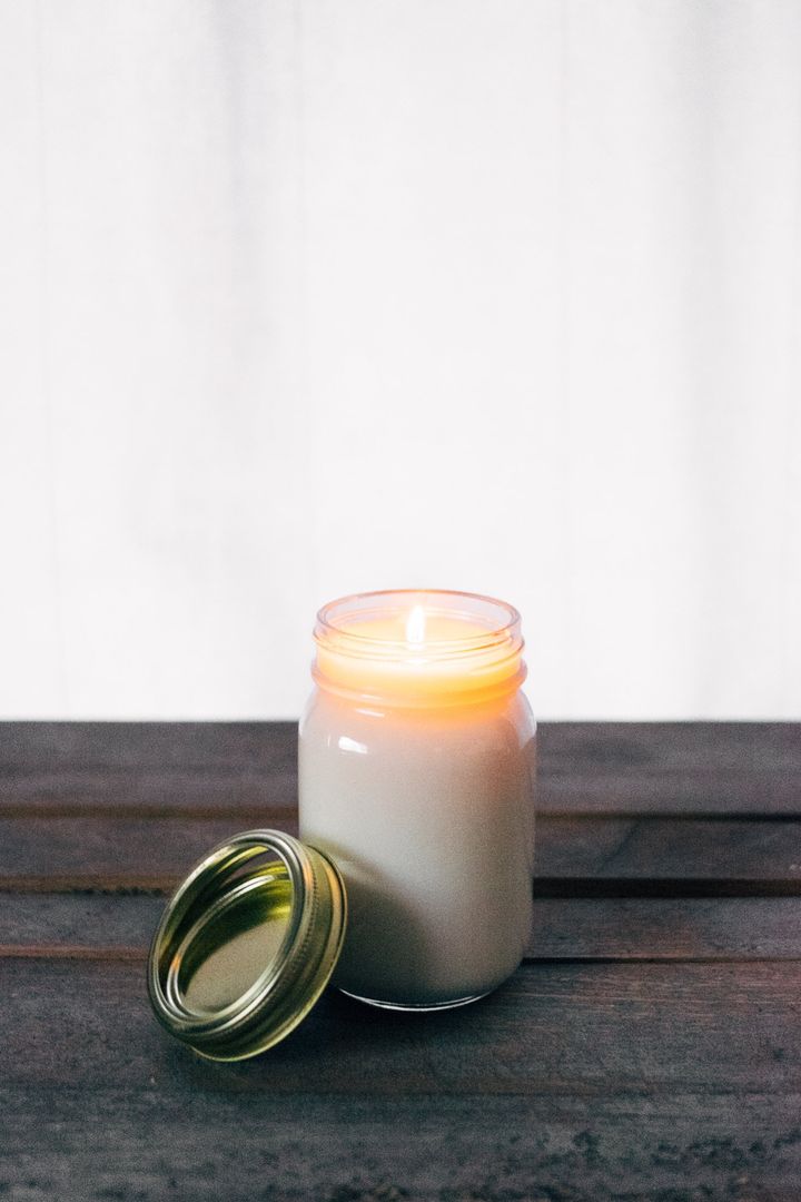 Glass Jar Candle Burning on Wooden Table with Lid