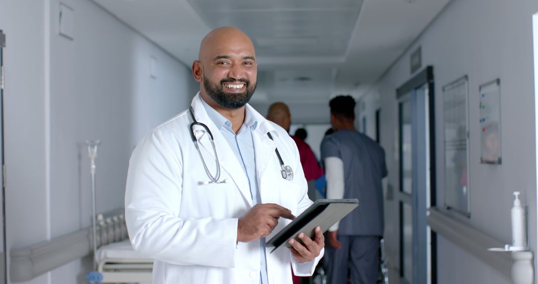 Smiling Doctor Holding Tablet in Hospital Corridor - Free Images, Stock Photos and Pictures on Pikwizard.com